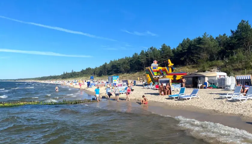 Plaża w Grzybowie pełna życia: dmuchany zamek, leżaki i tłumy plażowiczów cieszących się słońcem.