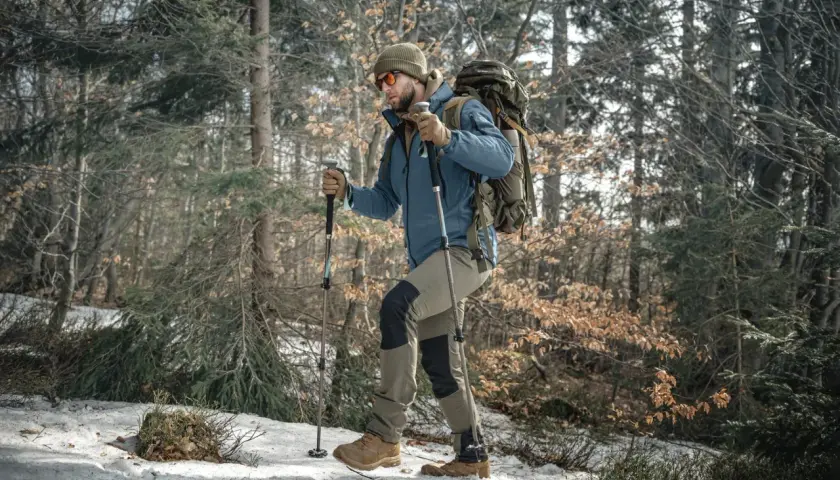 Mężczyzna z plecakiem i kije trekkingowe przemierza ośnieżony las.
