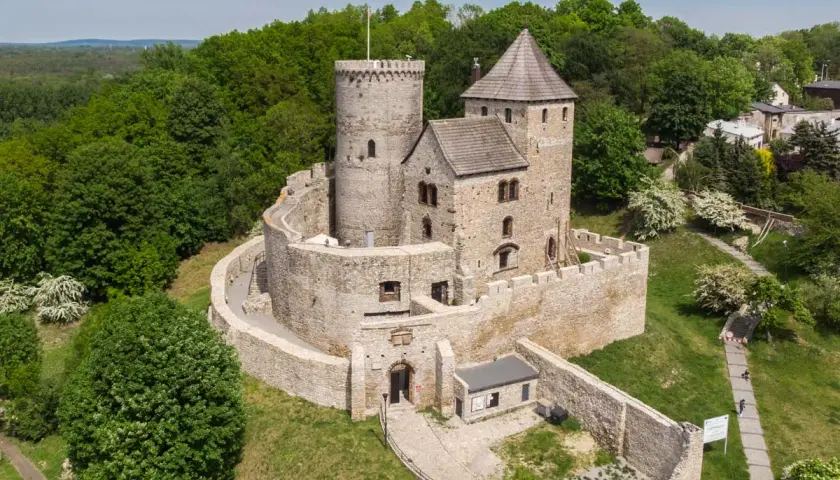 Kamienny zamek na wzgórzu, jeden z zamków piastowskich, otoczony zielenią.