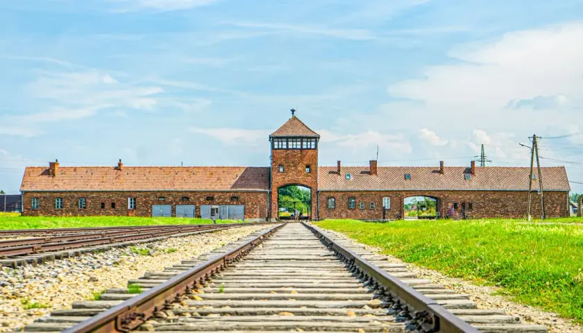 Brama obozowa w Oświęcimiu, z torami kolejowymi prowadzącymi do niej. Miejsce pamięci, które jest ważną częścią historii i atrakcją turystyczną.