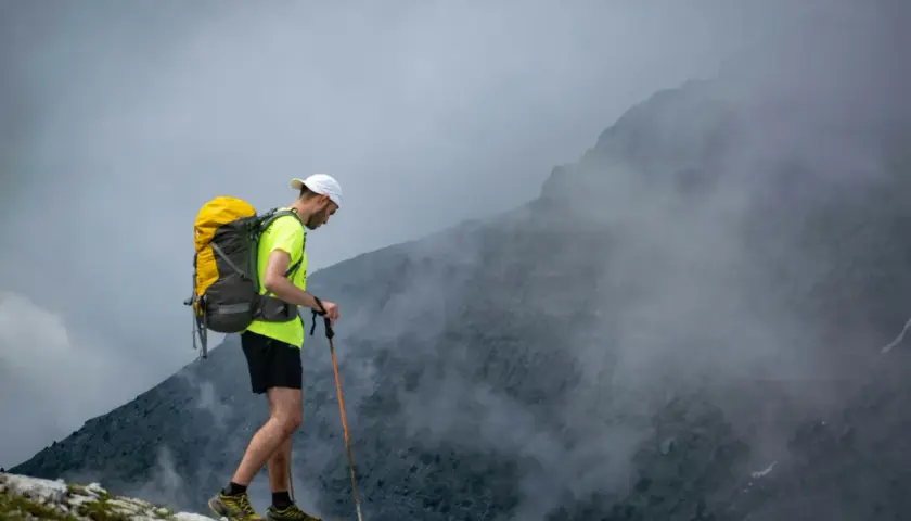 Mężczyzna z plecakiem i kijkami trekkingowymi wchodzi na mglisty szczyt. Wspaniały wyjazd w góry!