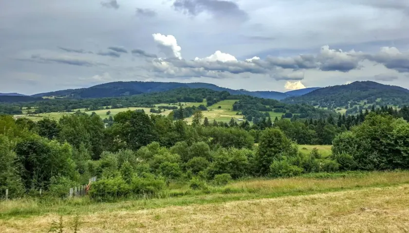Zielone wzgórza i lasy w Węgierskiej Górce zapraszają na piesze wędrówki. Widok na dolinę i chmury na niebie.
