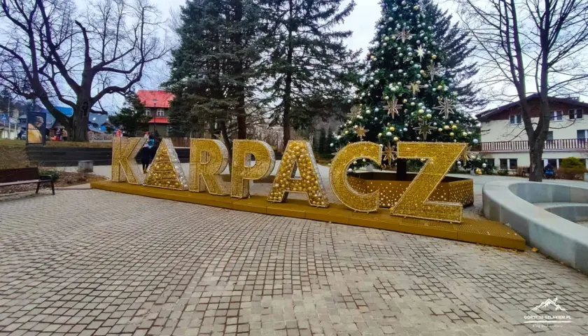 Złote litery KARPACZ w centrum, obok choinki, tworzą świąteczną atmosferę.