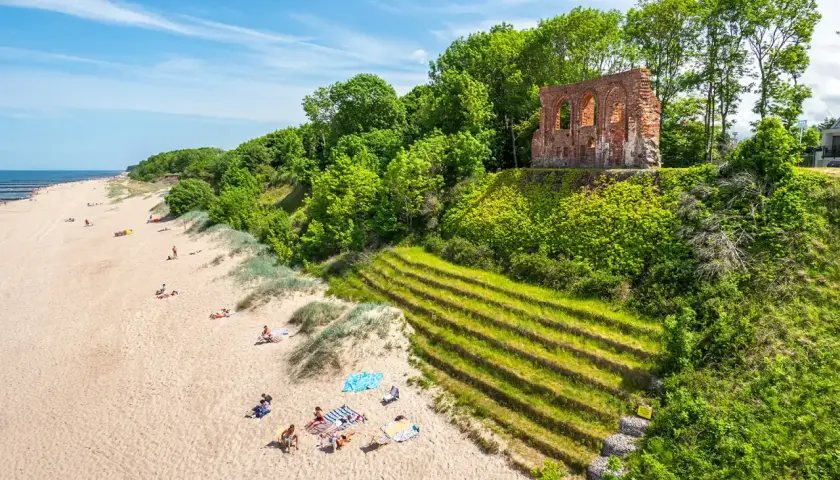 Piękna plaża z ruinami na wzgórzu, zielone zbocza i ludzie odpoczywający na piasku. Trzęsacz atrakcje zachwycają!
