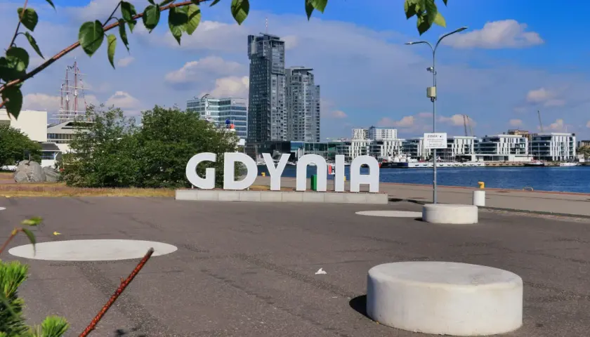 Napis GDYNIA na tle nowoczesnej architektury i żaglowca. Widok z Gdynia Rynek Główny.