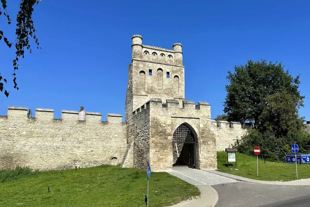 Kamienna brama z wieżą i murami obronnymi, jak z polskiego Carcassonne, w słoneczny dzień.
