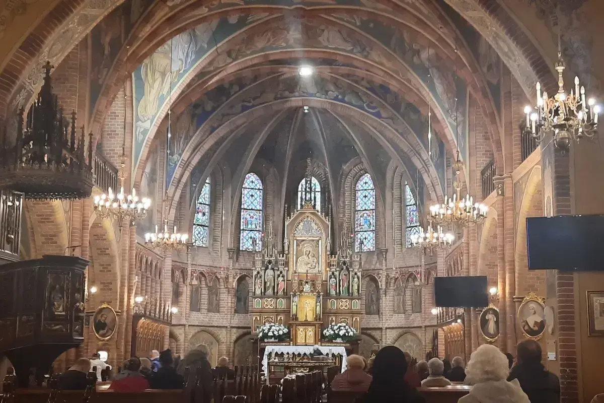 Wnętrze sanktuarium w Gietrzwałdzie, z ołtarzem głównym, witrażami i wiernymi na ławkach.