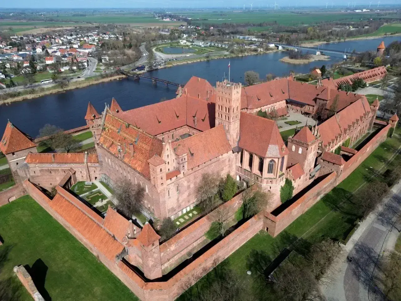 Potężny zamek w Malborku, jedna z największych atrakcji Polski, widziany z lotu ptaka. Rozległy kompleks z czerwonej cegły otoczony murami obronnymi, nad rzeką Nogat.
