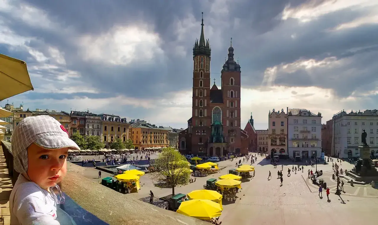 Małe dziecko na tle Rynku Głównego w Krakowie. Wspaniałe miejsce, by zobaczyć, co można robić w Krakowie: zwiedzać, spacerować, podziwiać architekturę.