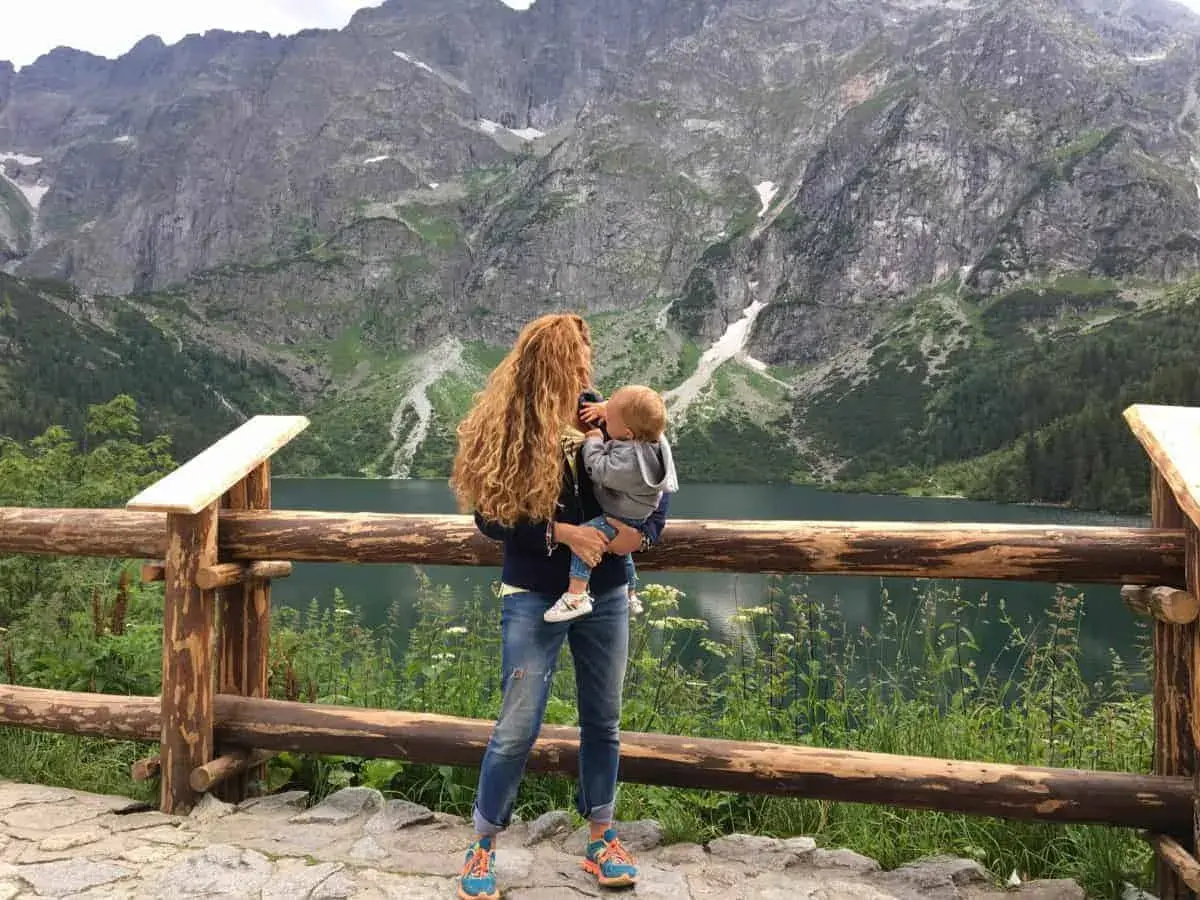 Kobieta z dzieckiem na rękach podziwia malowniczy widok Tatr. Wspaniałe **Zakopane z wózkiem** to idealne miejsce na rodzinne wycieczki.