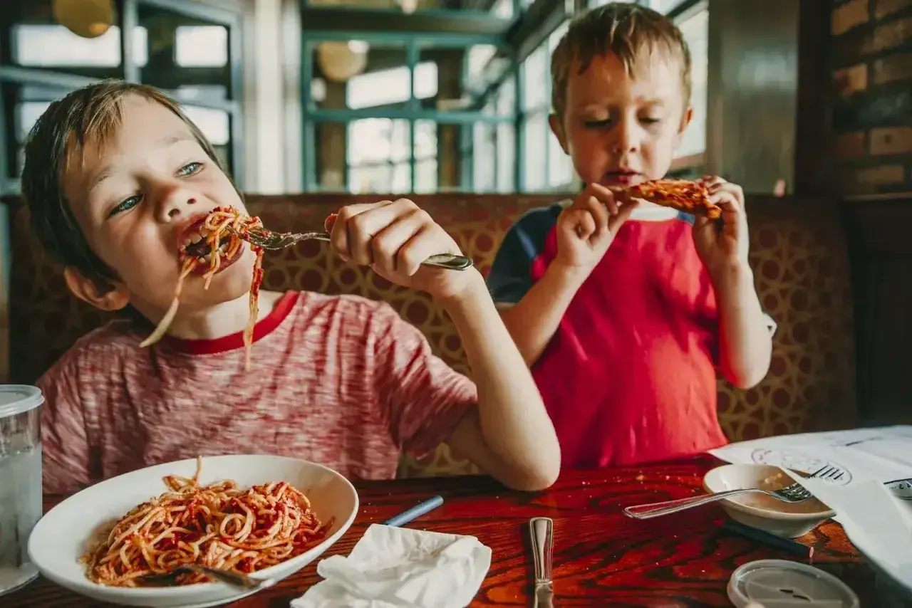 Dwóch chłopców zajada spaghetti i pizzę. Szukasz miejsca, gdzie zjeść w Kołobrzegu?