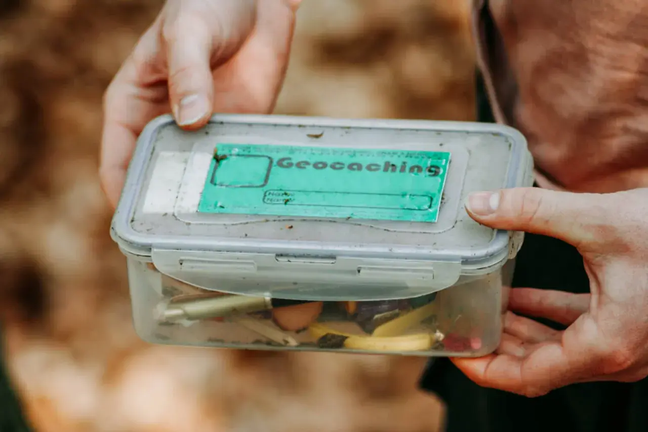 Pudełko z napisem "Geocaching" i drobiazgami w środku. To świetna zabawa, która polega na szukaniu ukrytych skarbów.