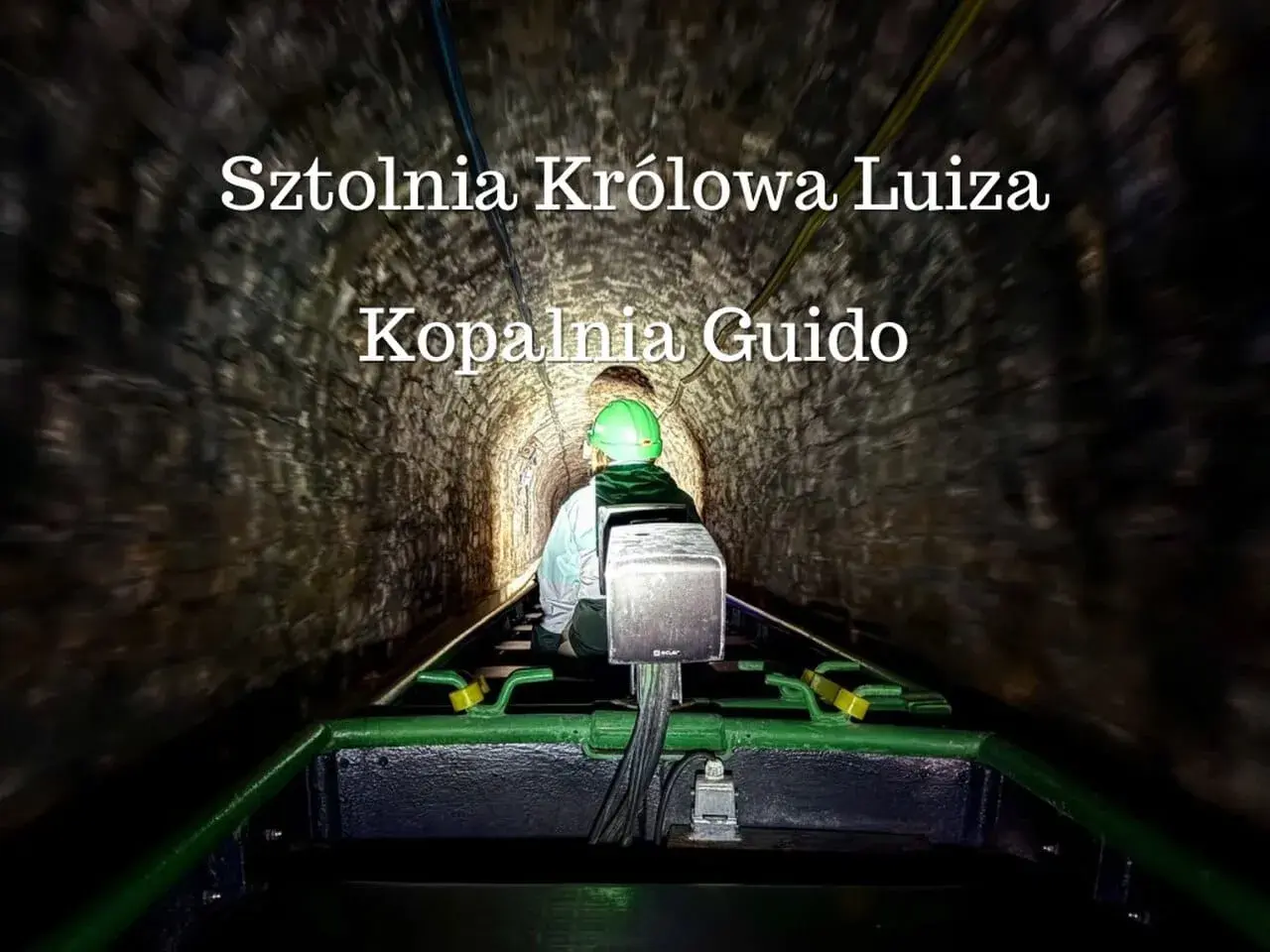 Osoba w kasku jedzie kolejką w ciemnej sztolni Królowa Luiza, Kopalnia Guido.