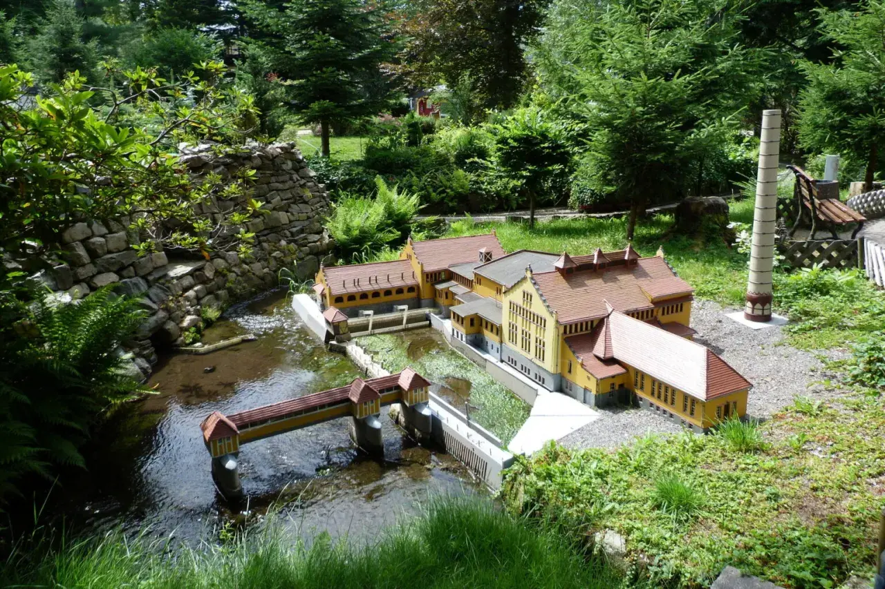 Miniaturowa zabudowa z mostkiem i rzeką, jak w parkach miniatur w Polsce.