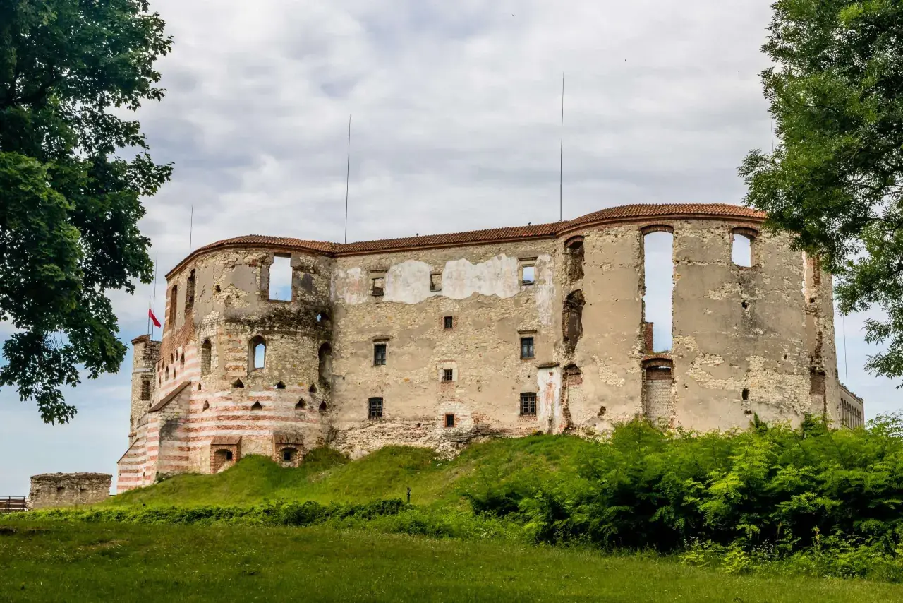 Zamek w Janowcu, ruiny zamku z czerwono-białymi pasami na wieży, otoczone zielenią.