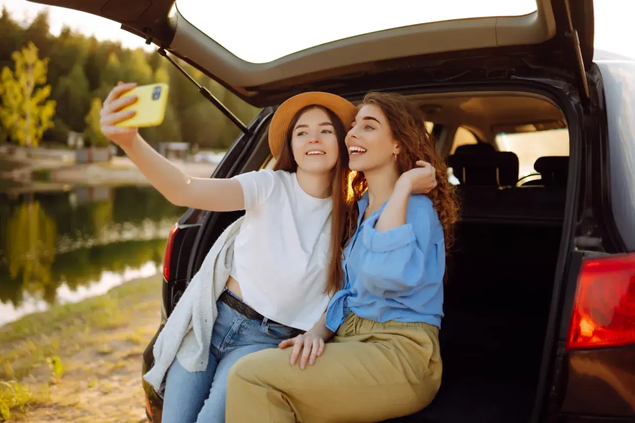 Dwie przyjaciółki robią sobie selfie przy samochodzie nad jeziorem. Idealny weekend z przyjaciółką!