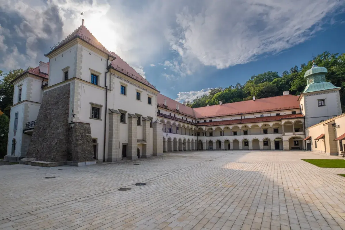 Zamek w Suchej Beskidzkiej z dziedzińcem i arkadowymi krużgankami. W tle zielone wzgórza.