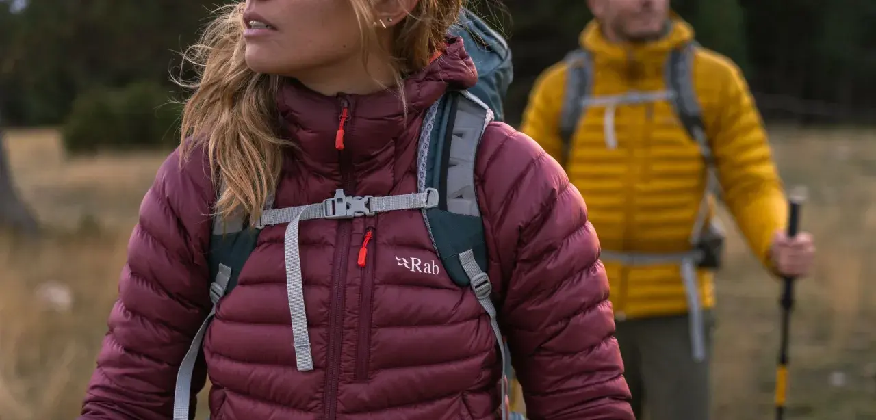 Dwie osoby w kurtkach puchowych Rab, gotowe na wędrówkę. Rab to firma tworząca odzież outdoorową.