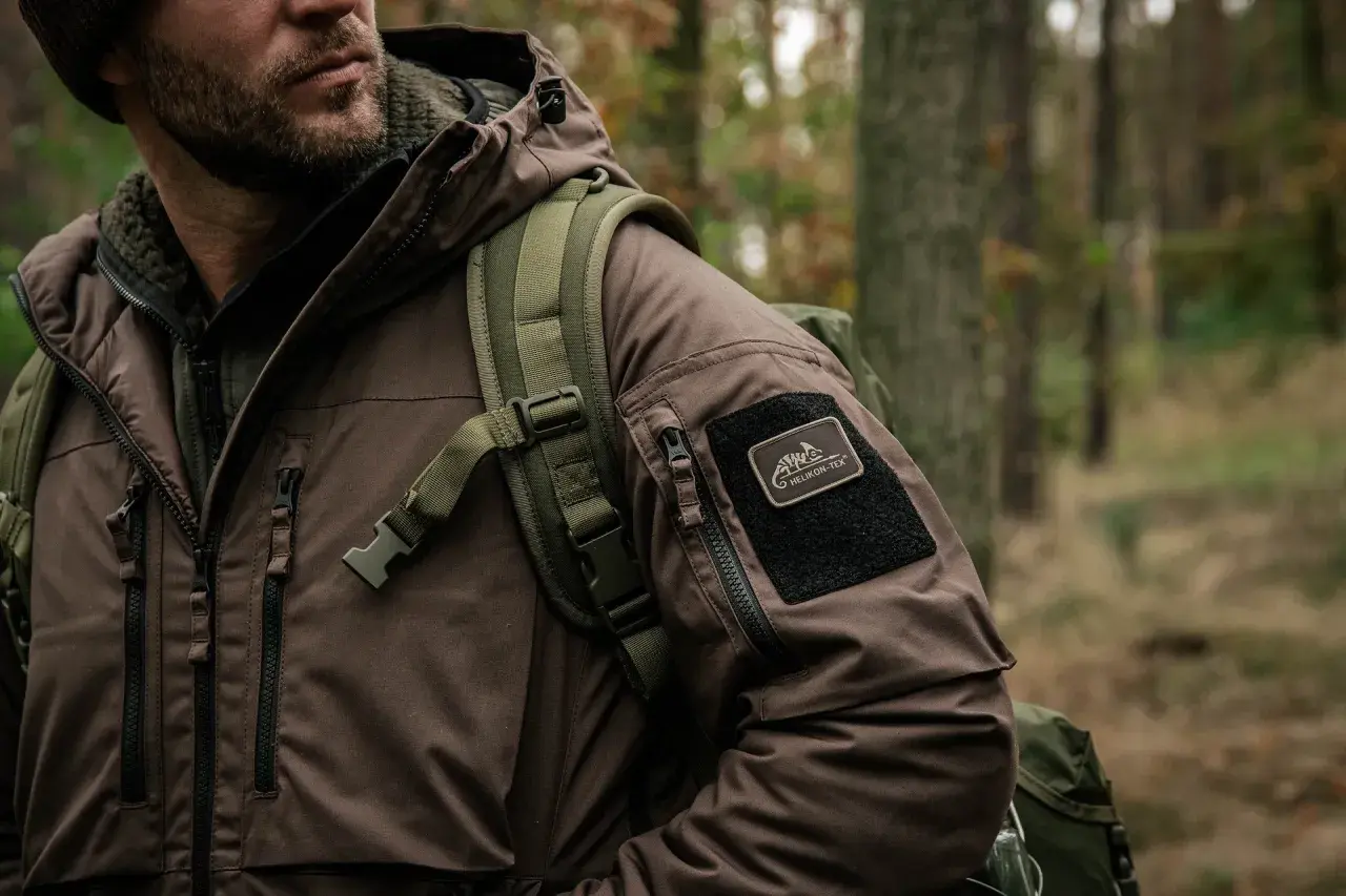 Mężczyzna w brązowej kurtce z naszywką Helikon-Tex, gotowy na przygodę. To dowód, że polskie marki outdoorowe to jakość i styl.