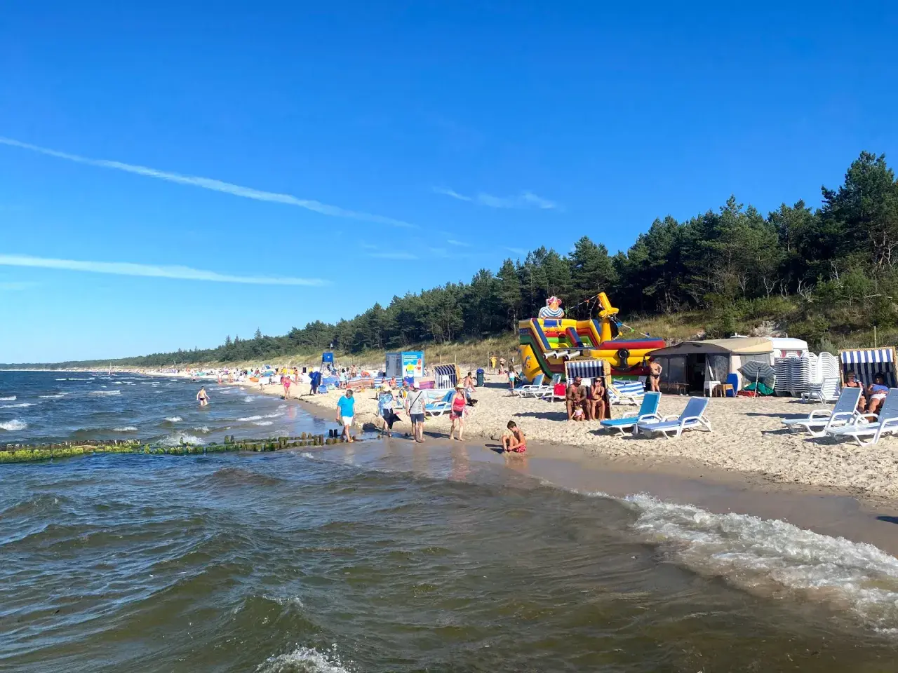 Plaża w Grzybowie pełna życia: dmuchany zamek, leżaki i tłumy plażowiczów cieszących się słońcem.