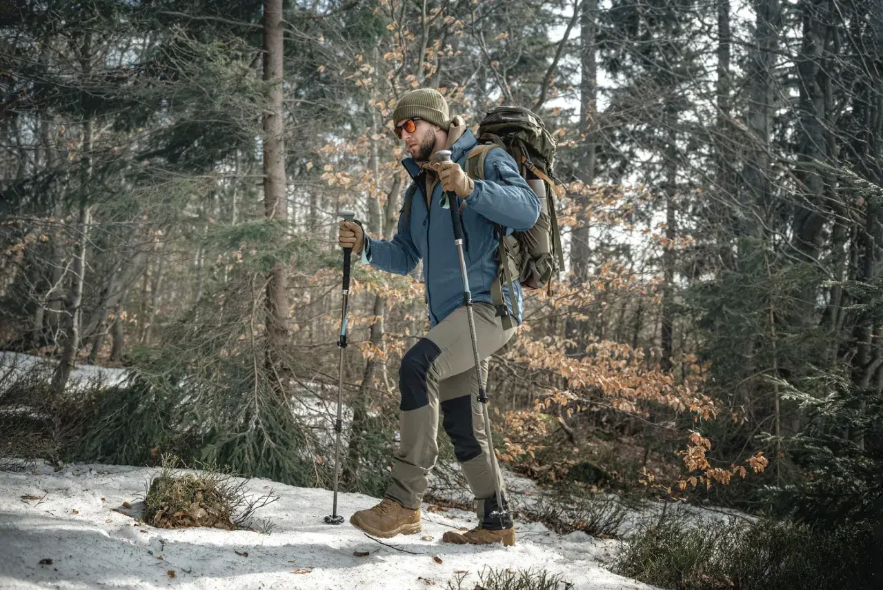 Mężczyzna z plecakiem i kije trekkingowe przemierza ośnieżony las.