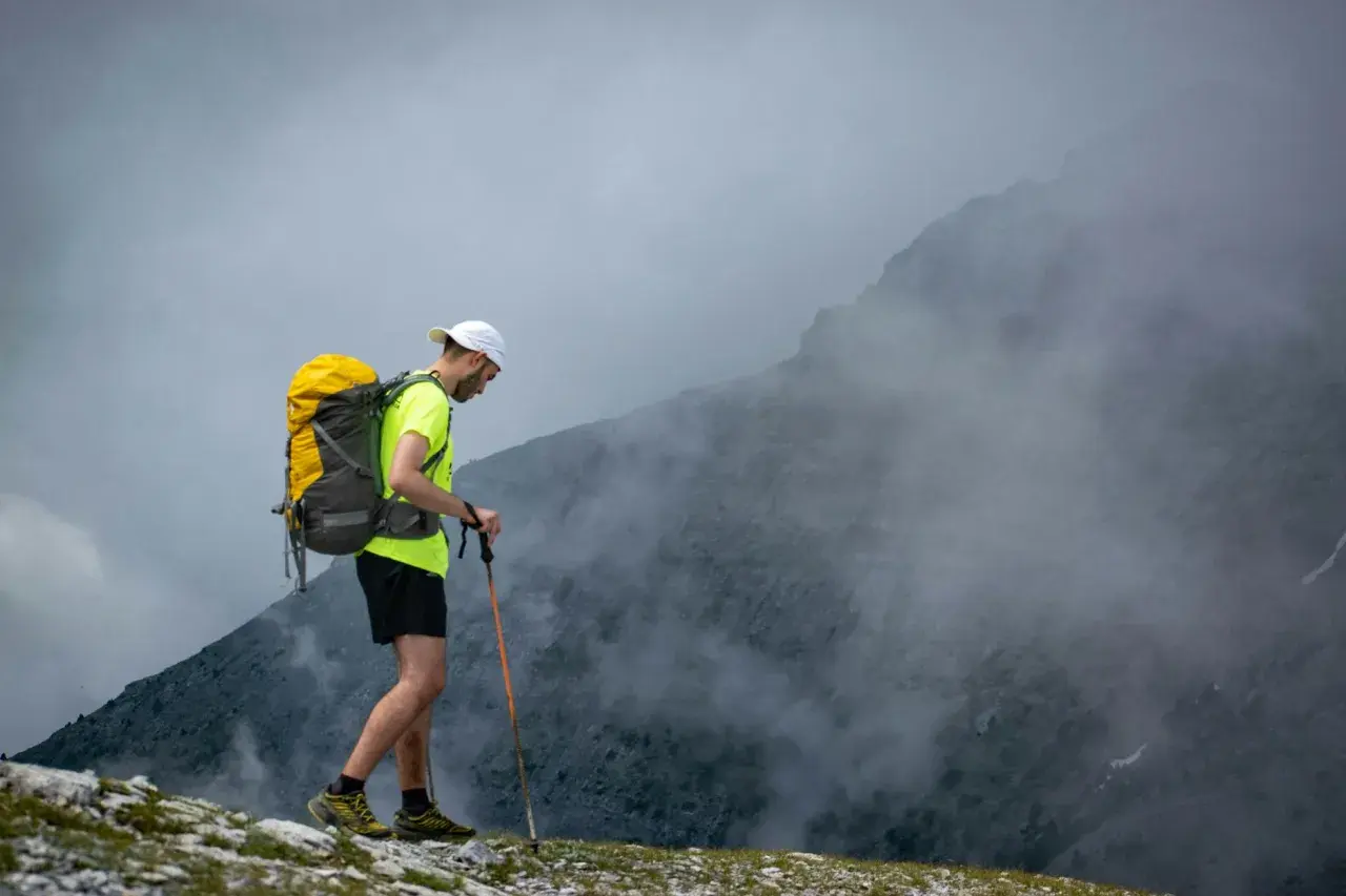 Mężczyzna z plecakiem i kijkami trekkingowymi wchodzi na mglisty szczyt. Wspaniały wyjazd w góry!
