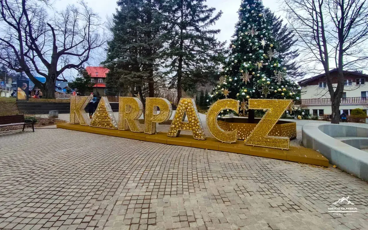 Złote litery KARPACZ w centrum, obok choinki, tworzą świąteczną atmosferę.