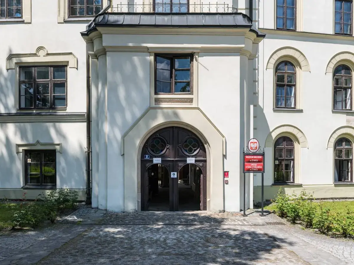 Wejście do zabytkowego zamku w Żywcu, z charakterystycznymi drzwiami i oknami. Obok tablica informująca o Muzeum Miejskim i Urzędzie Stanu Cywilnego.