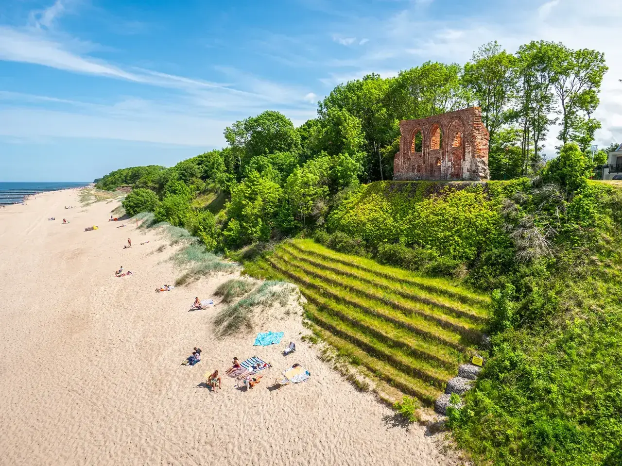 Piękna plaża z ruinami na wzgórzu, zielone zbocza i ludzie odpoczywający na piasku. Trzęsacz atrakcje zachwycają!