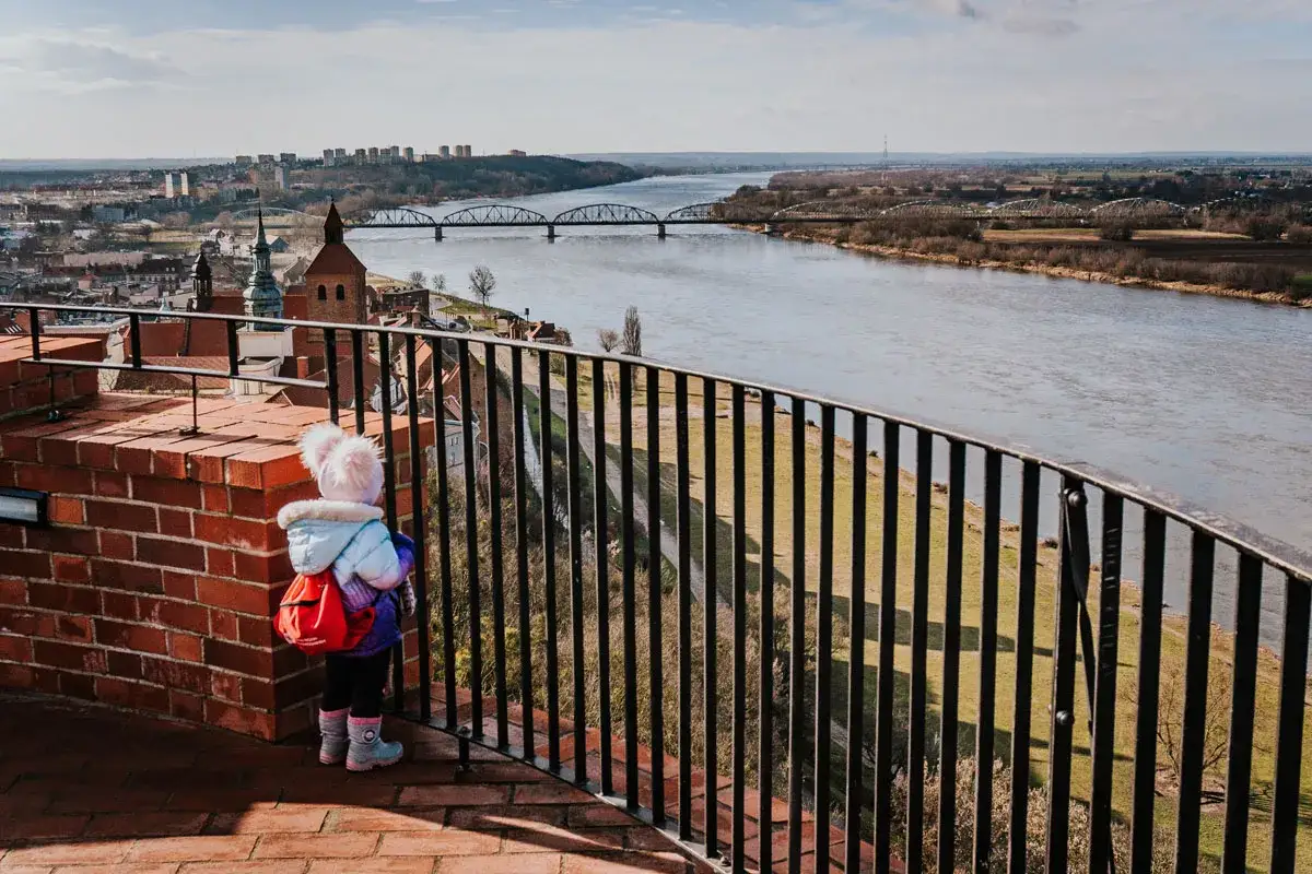 Dziecko z plecakiem podziwia panoramę Grudziądza i Wisły. Widok na mosty i miasto to jedne z głównych atrakcji.