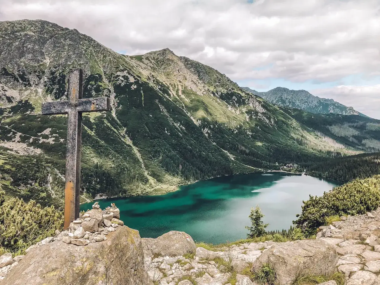 Kamienny krzyż na tle gór i jeziora Morskie Oko. Widok na najwyższy szczyt w Polsce, Rysy, w oddali.