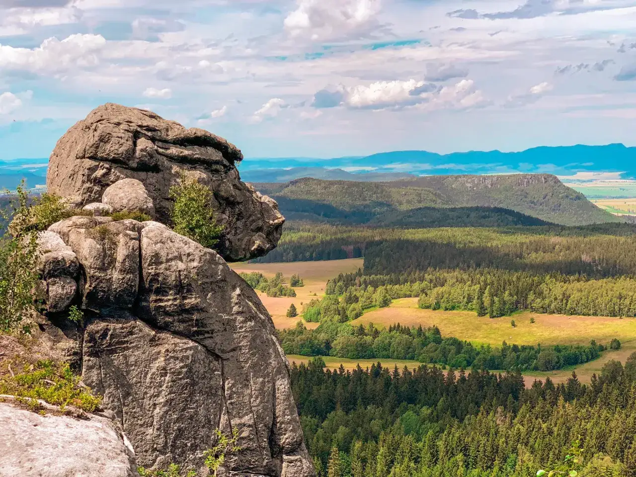 Skaliste formacje na pierwszym planie, a w tle rozległe, zielone góry stołowe Polska. Widok zapiera dech w piersiach.