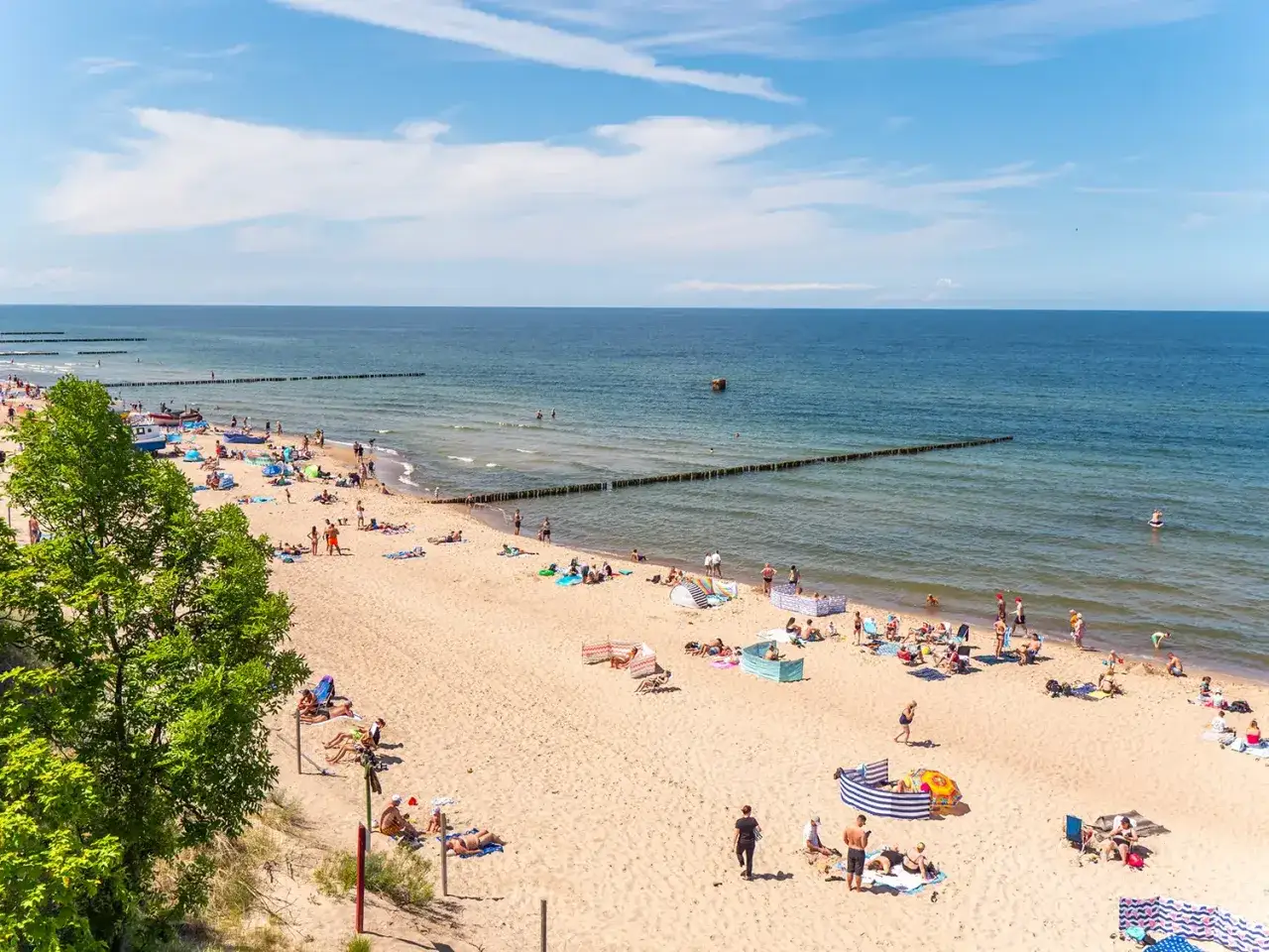Słoneczna plaża w Rewalu pełna ludzi, którzy korzystają z uroków lata. To jedne z głównych rewal atrakcje.