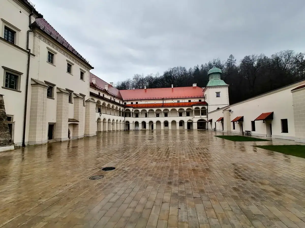 Zamek w Suchej Beskidzkiej, z mokrym dziedzińcem i arkadowymi krużgankami, otoczony lasem.