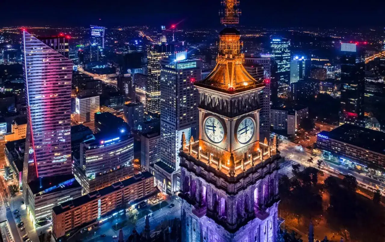 Warszawa nocą: Pałac Kultury i Nauki z zegarami, nowoczesne wieżowce, światła miasta. Idealne warszawa atrakcje dla dorosłych szukających wrażeń.