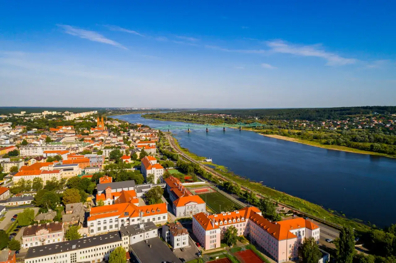 Widok na miasto nad Wisłą z zielonym mostem i licznymi budynkami z czerwonymi dachami.
