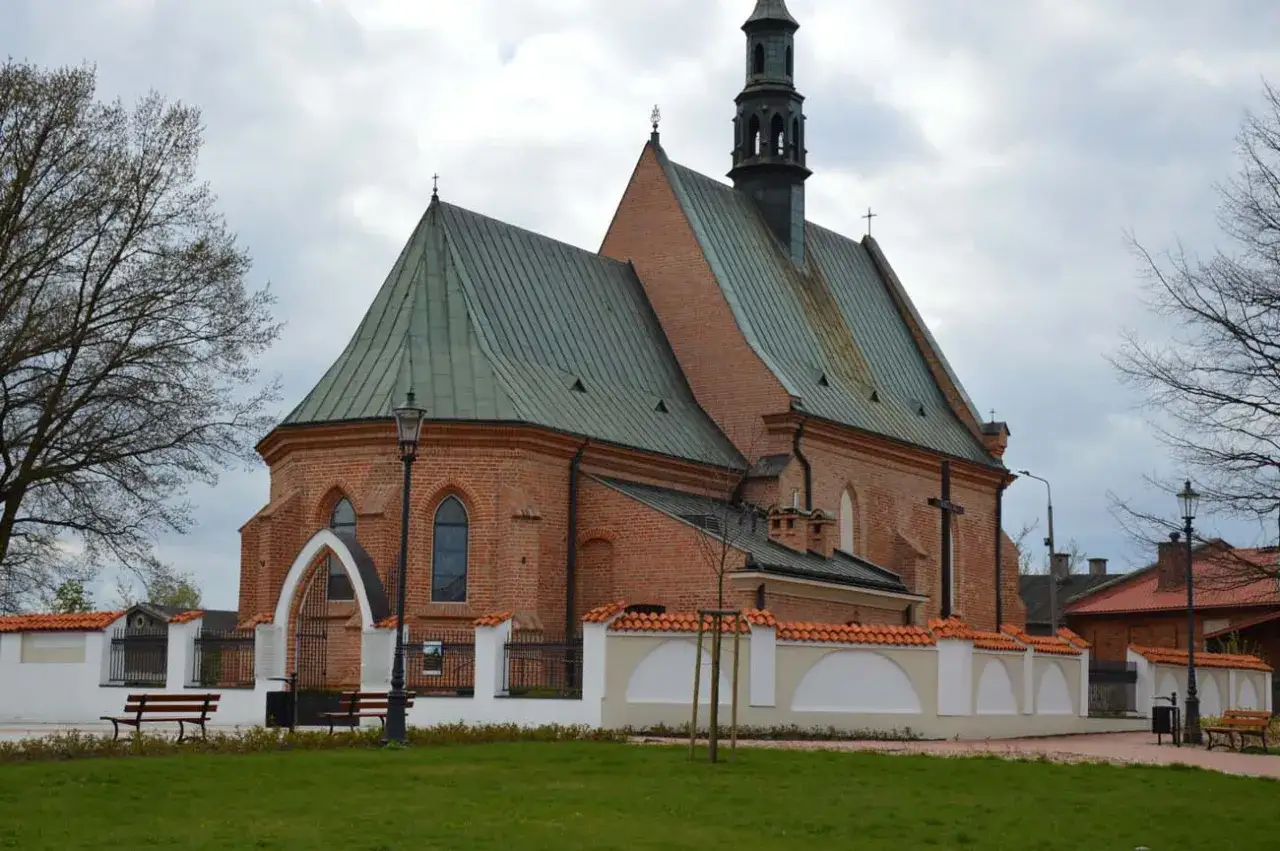 Gotycka ceglana świątynia z wieżyczką, otoczona murem i zielenią. Jedna z radomskich atrakcji, idealna na spokojny spacer.