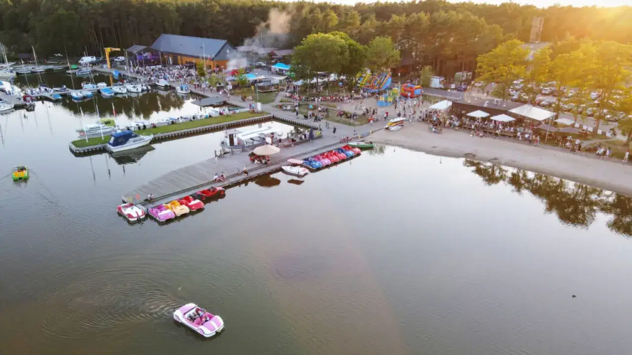Dąbki atrakcje: plaża, marina z łódkami, dmuchańce i mnóstwo ludzi cieszących się letnim dniem nad jeziorem.