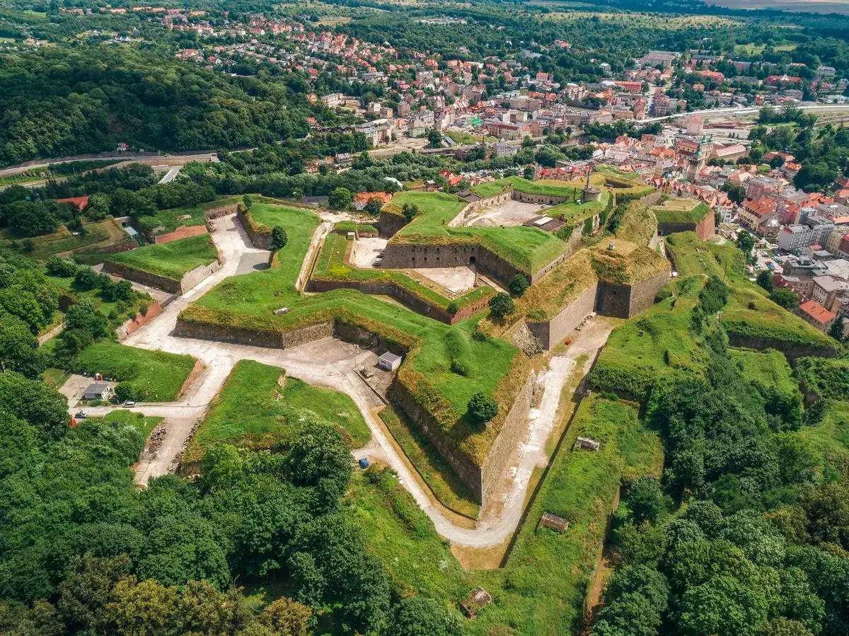 Imponująca twierdza w Kłodzku, jedna z największych atrakcji regionu, rozciąga się na wzgórzu, otoczona zielenią i miastem.
