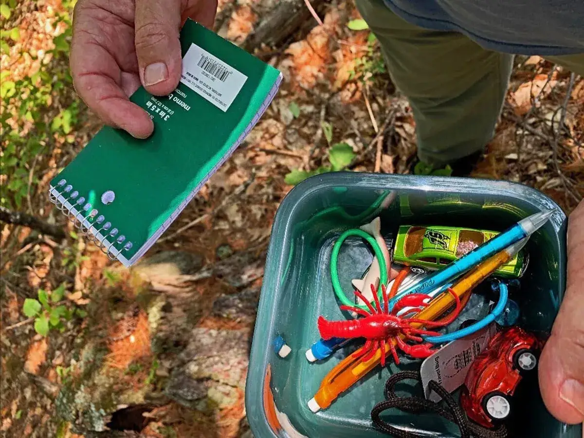 Odkrywanie skarbów w lesie, czyli geocaching co to. W pojemniku zabawki, długopisy i notatnik do zapisywania znalezisk.