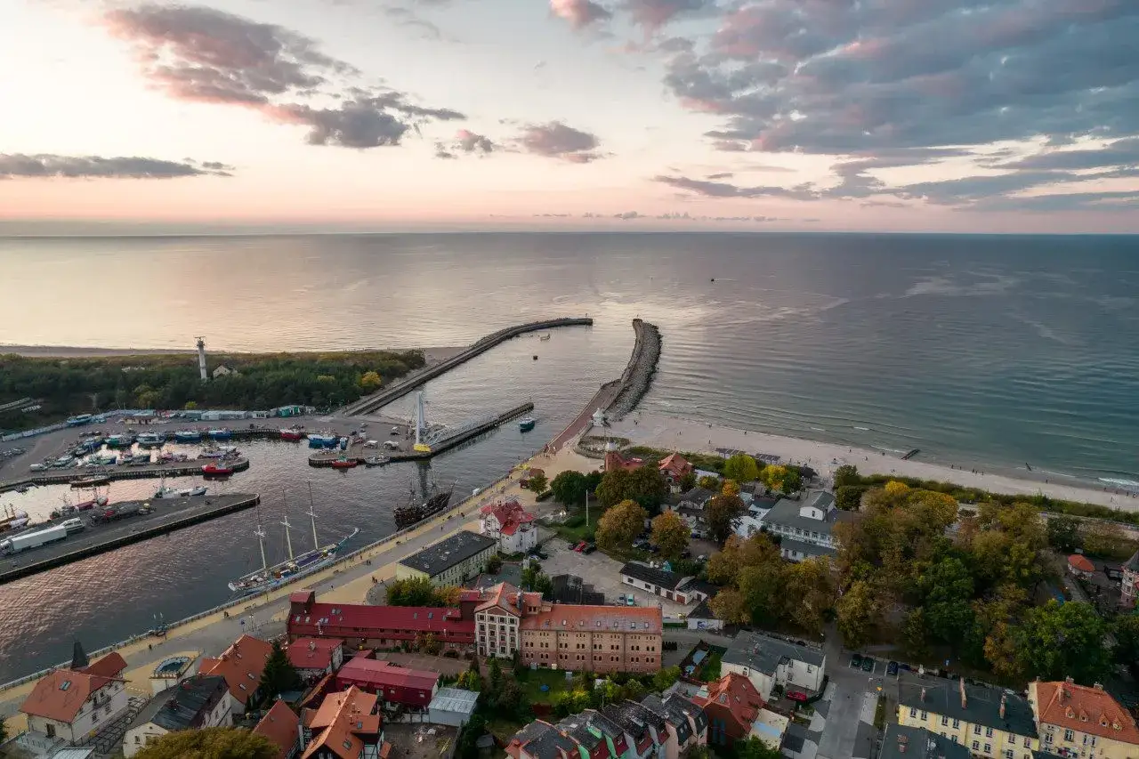 Widok z lotu ptaka na port i plażę w Ustce. Widać łodzie, latarnię morską i zabudowania. To wspaniałe ustka atrakcje.