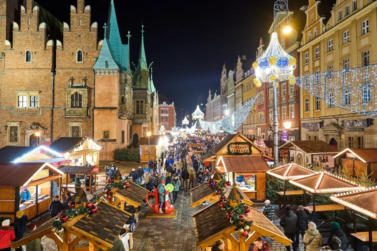 Tłum ludzi na największym jarmarku bożonarodzeniowym w Polsce. Kolorowe kamienice, świąteczne iluminacje i drewniane kramy tworzą magiczną atmosferę.