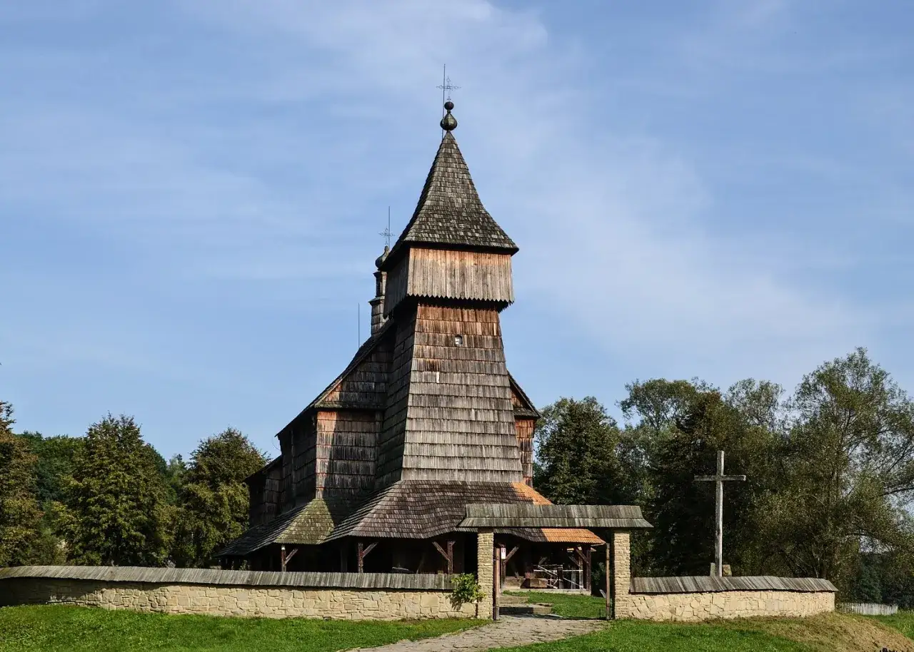 Drewniana cerkiew w skansenie Sanok, z charakterystyczną wieżą i kamiennym murem.