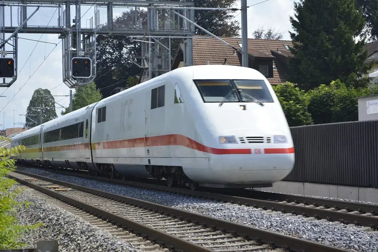 Biały pociąg ICE z czerwonym pasem jedzie po torach. To symbol turystyki zrównoważonej, która pozwala odkrywać świat w ekologiczny sposób.