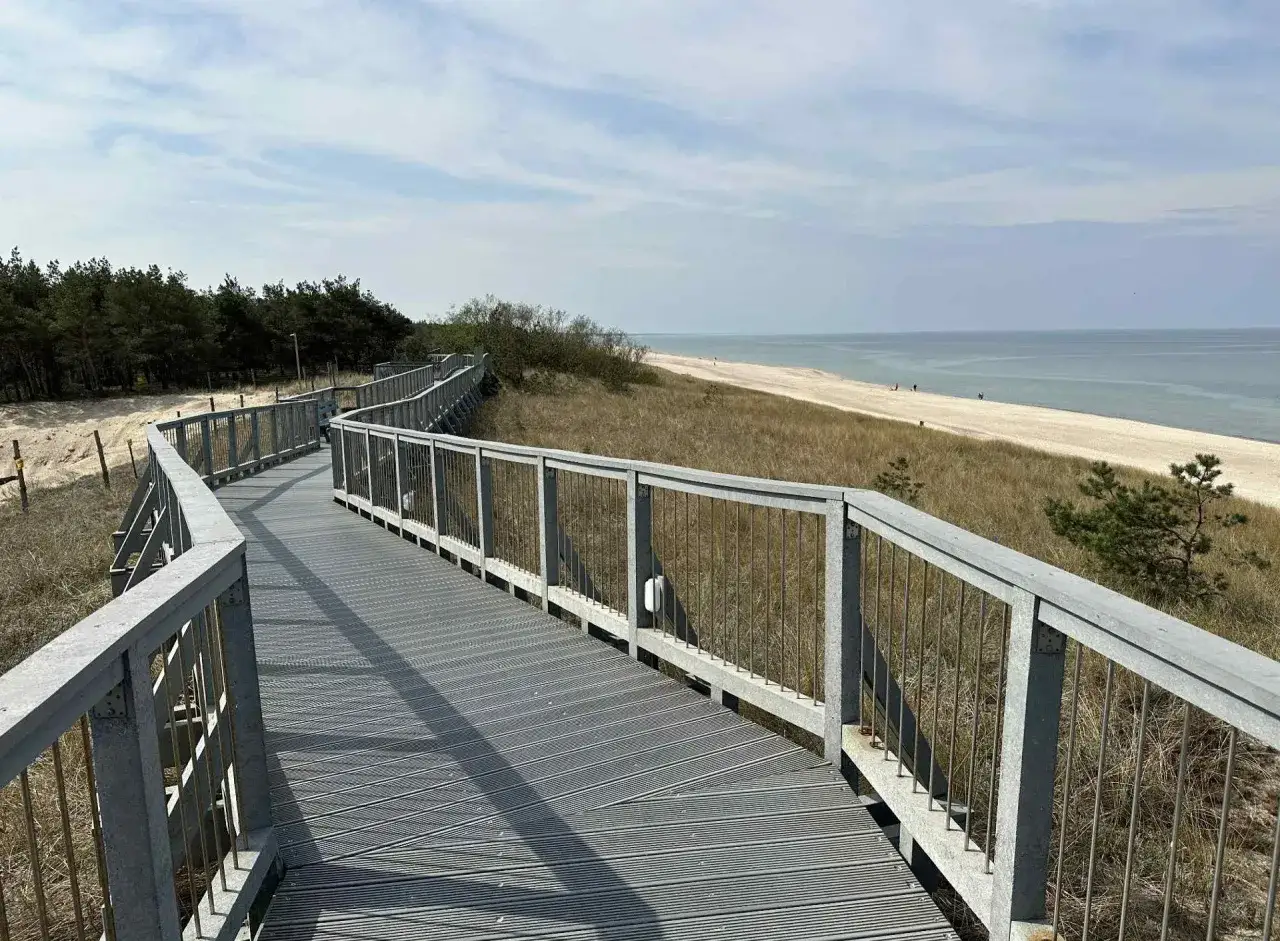 Drewniana promenada nad morzem prowadzi przez wydmy do piaszczystej plaży.