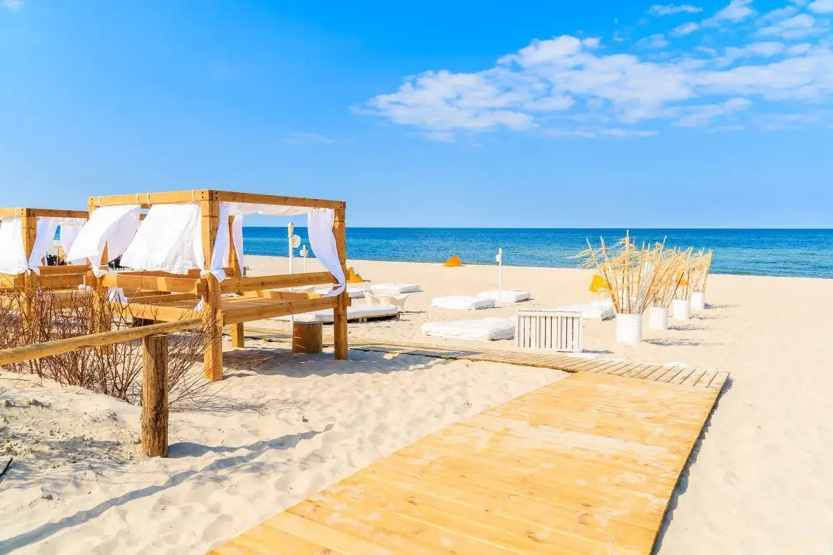 Jastarnia atrakcje: drewniane altany i leżaki na piaszczystej plaży, z widokiem na spokojne morze i błękitne niebo.