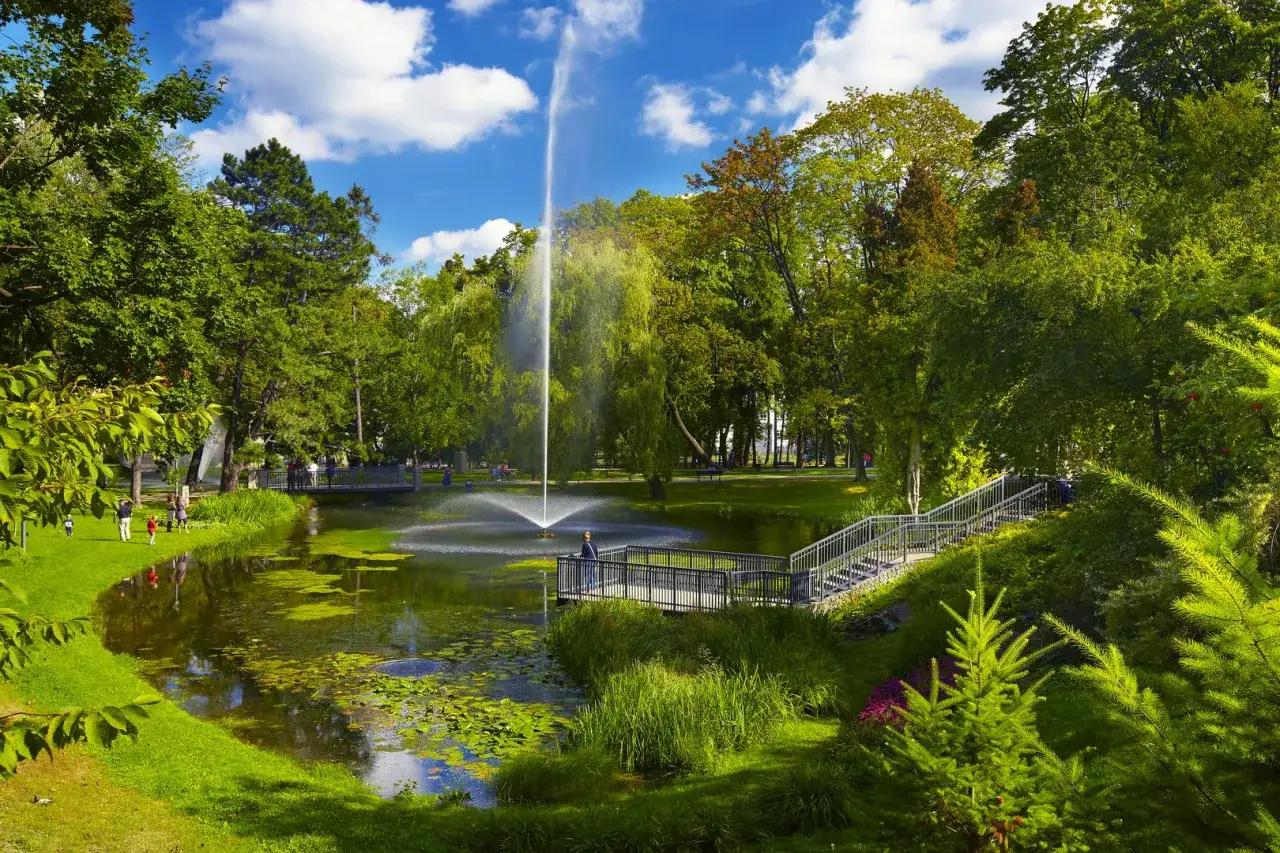 Park z fontanną i stawem, zielone drzewa, ścieżki i mostki. Wspaniałe częstochowa atrakcje dla każdego.