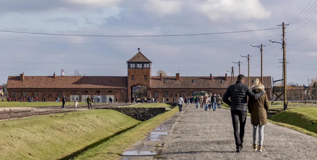 Odwiedzający teren byłego obozu Auschwitz-Birkenau, gdzie znajdują się ważne historycznie atrakcje. Para spaceruje ścieżką w kierunku bramy.