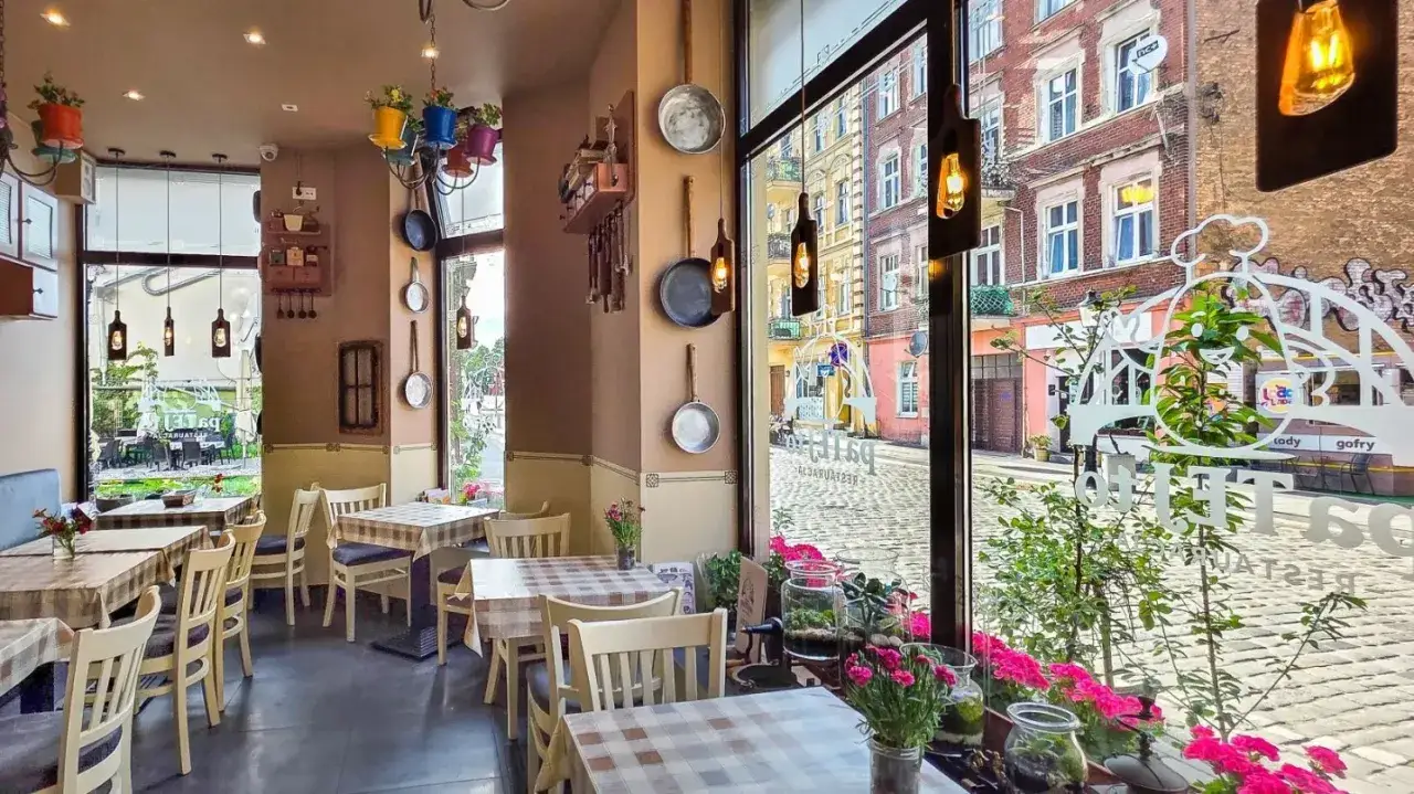 Przytulne wnętrze restauracji z kratowanymi obrusami i wiszącymi patelniami. Idealne miejsce na posiłek wśród polecanych restauracji Poznań.