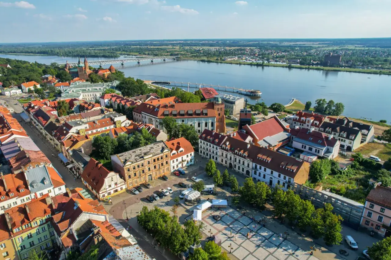 Widok na Wisłę i zabytkowe centrum Płocka. Widać katedrę, most kolejowy i urokliwe kamienice, które tworzą niepowtarzalne atrakcje Płocka.